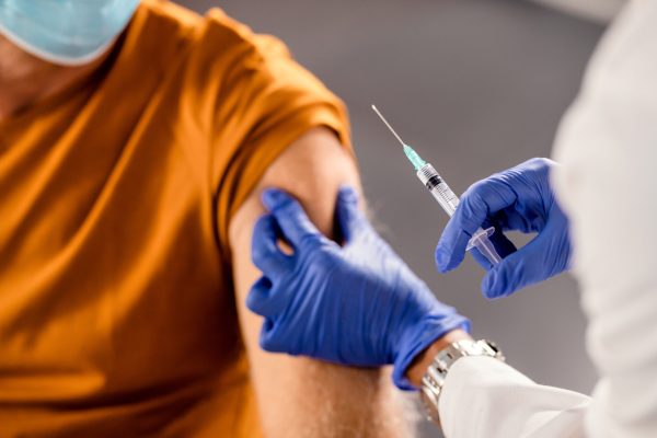 Close-up of a doctor vaccinating senior man in the hospital during coronavirus pandemic.