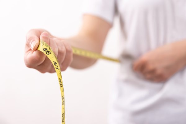 A woman in a white t-shirt holds a yellow centimeter tape in her hands. The concept of losing weight, gaining weight.